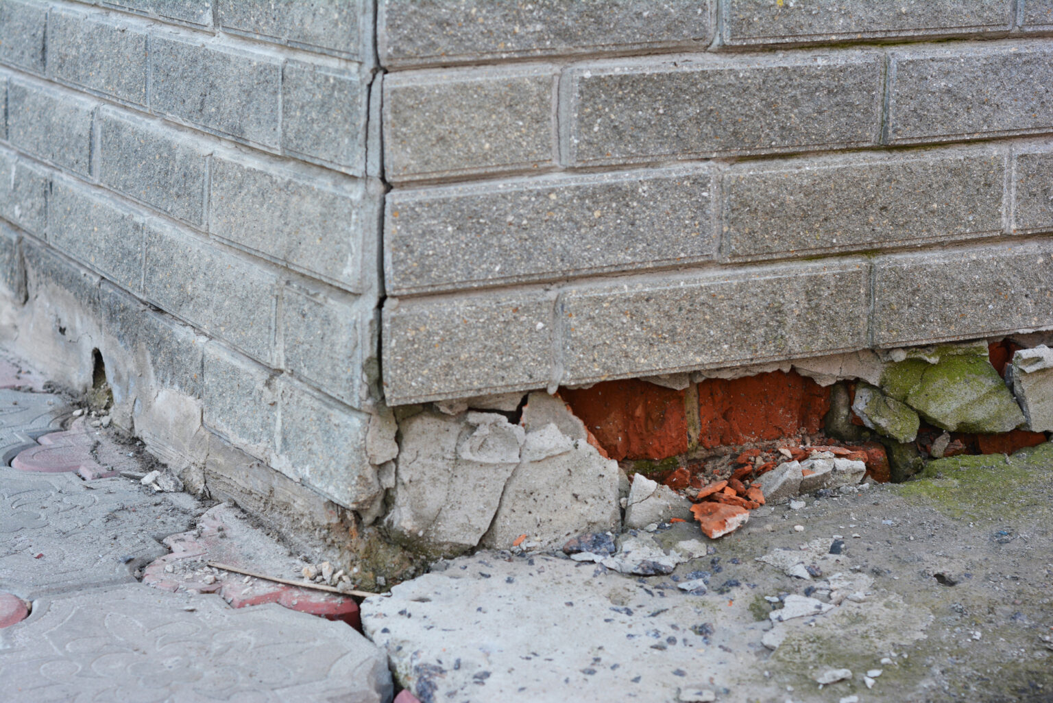 Photo of a cracked/crumbling grey brick foundation.